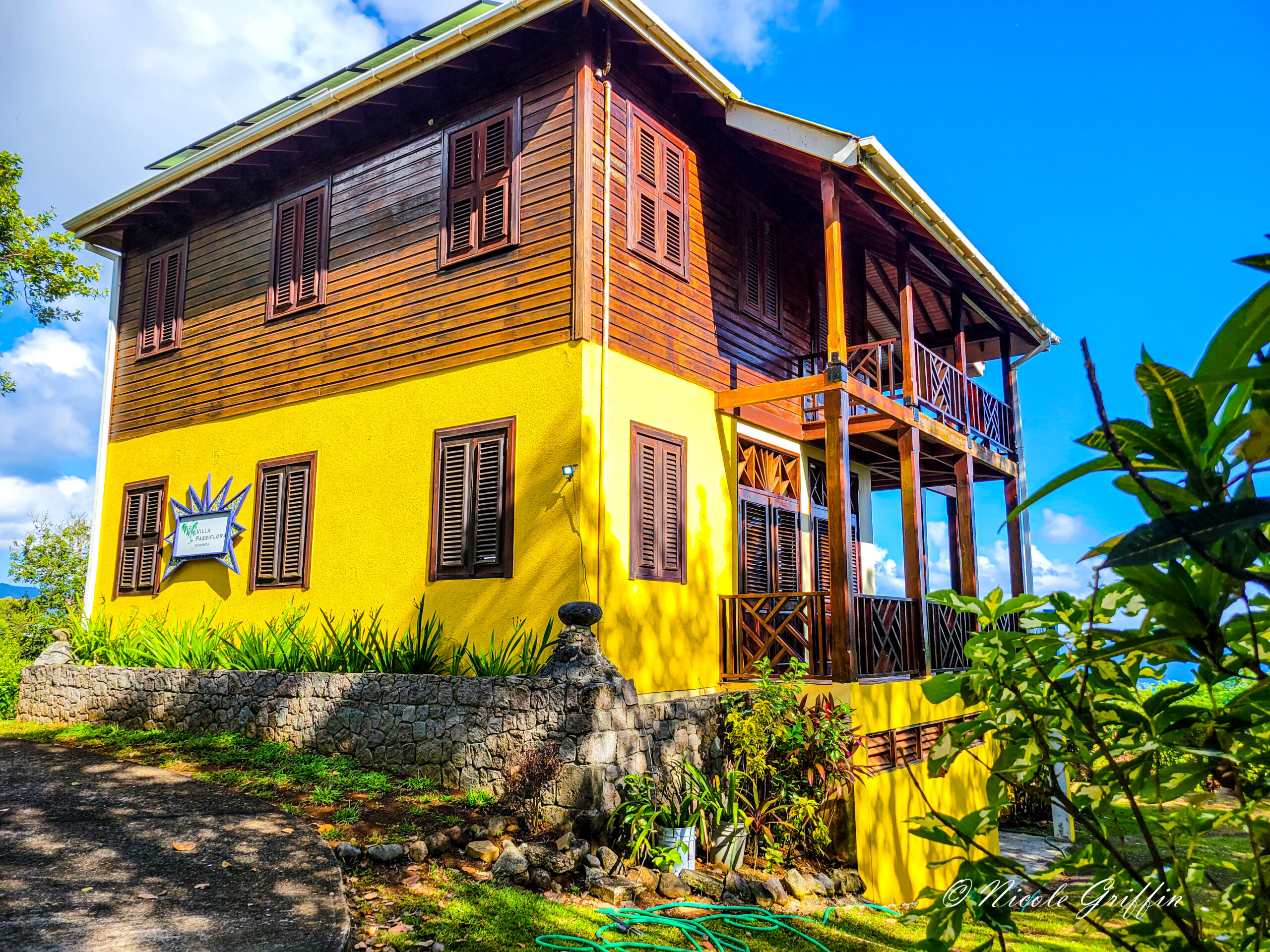 A wooden and yellow two-story house surrounded by greenery